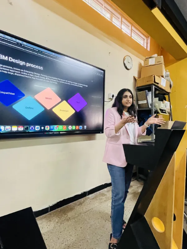 Nanditha presenting next to a large screen in an office.