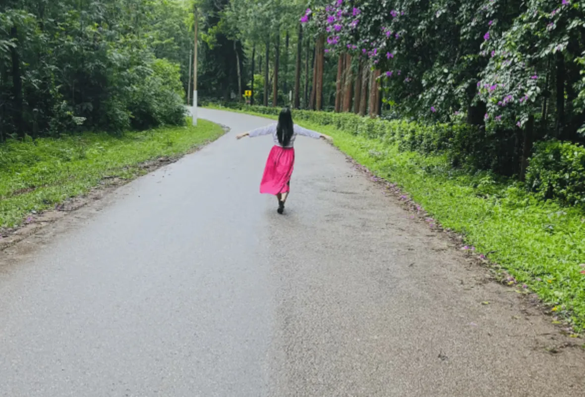 Nanditha walking down an empty road through a forest.