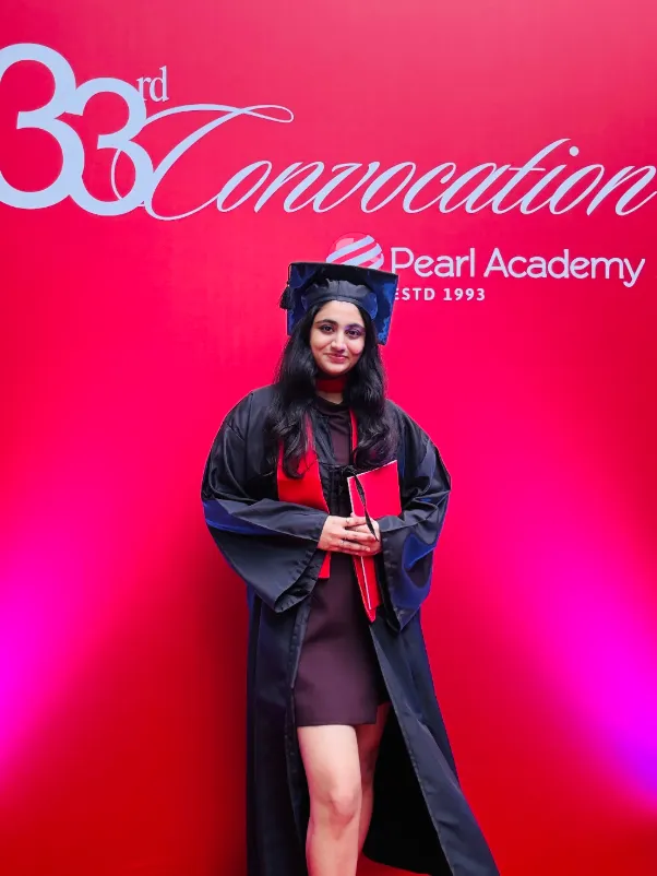 Nanditha in her graduation gown in front of the convocation backdrop.